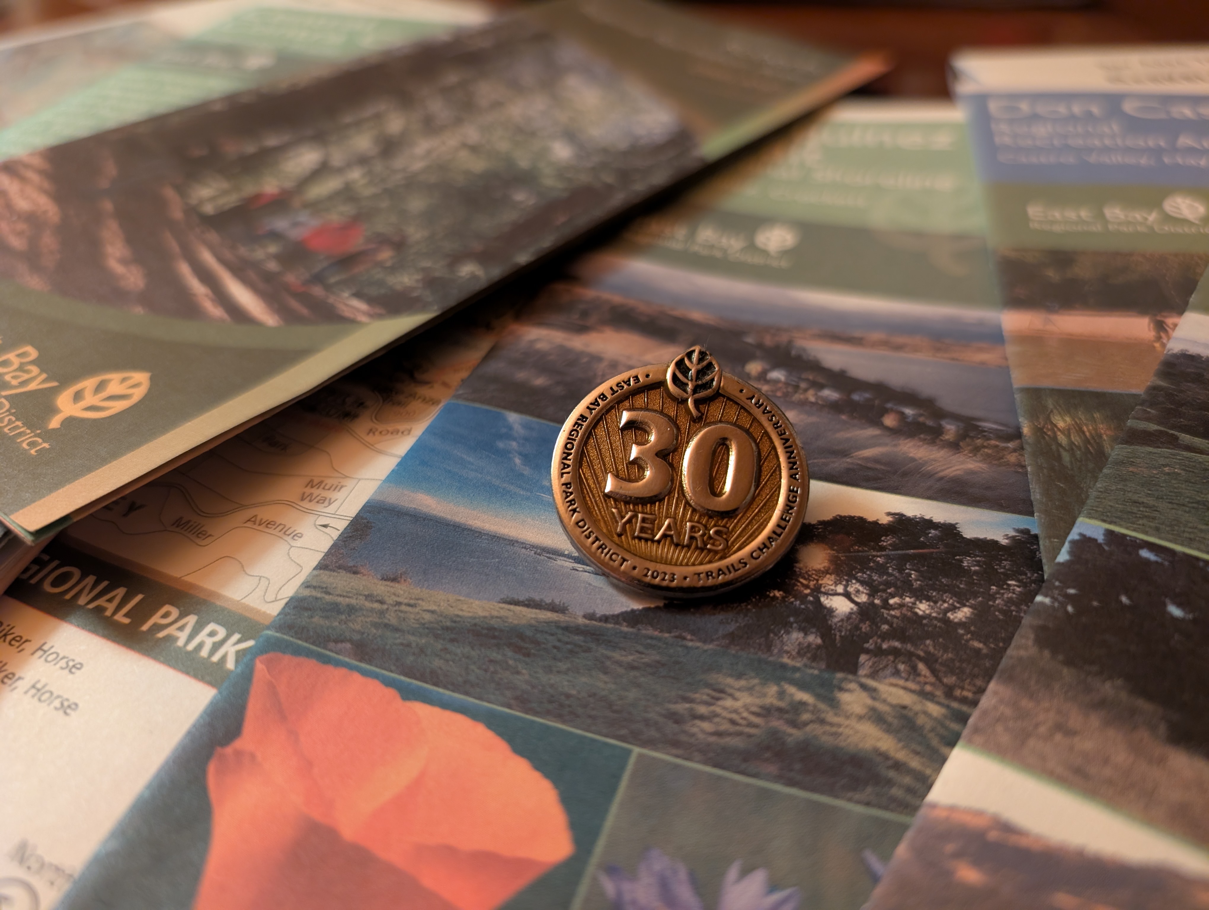 A Trails Challenge pin atop various East Bay Parks maps